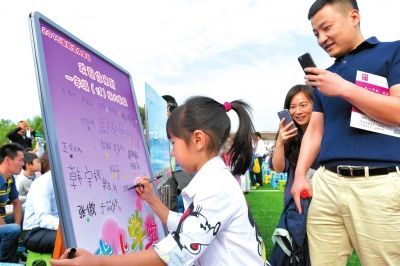 中关村二小百旺校区新学年开学，一年级新生在签名牌上写下名字，她的爸爸妈妈“各种拍”。　京华时报记者王海欣摄